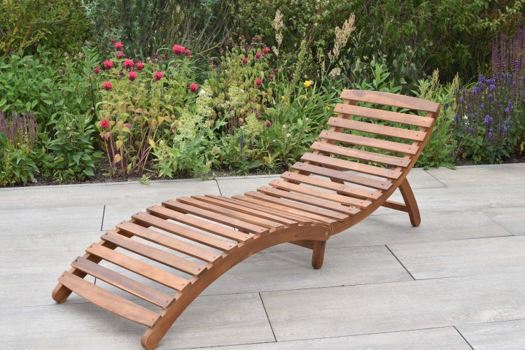 Holzliege im Garten vor blühenden Pflanzen