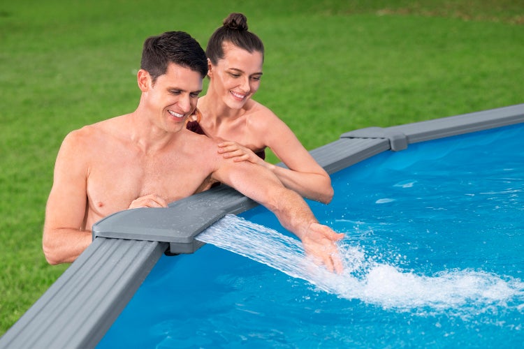 Ein Paar am Rand eines Swimmingpools mit integriertem Wasserfall in einem Garten.