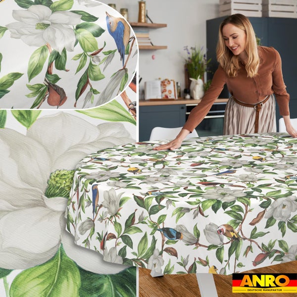 Runde Tischdecke mit Blumenmuster, weißen Blüten, grünen Blättern und bunten Vögeln in einer Küche. ANRO Logo.