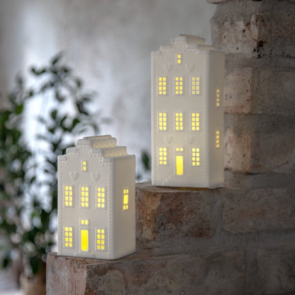 Zwei dekorative Häuser aus Keramik mit Fenster- und Türöffnungen für Teelichter auf einer Steinstufe