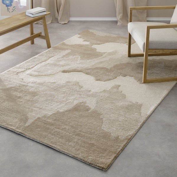 Moderner Teppich mit abstraktem Muster in einem hellen Raum mit Holzbank, Sessel und Boden in Betonoptik.