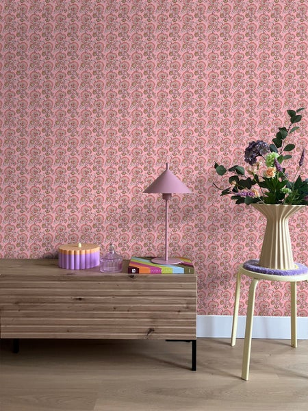 Ein Zimmer mit einer Kommode, einem Stuhl und einer mit Blumenmuster versehenen Tapete