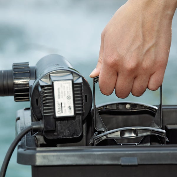 Eine Hand hebt den Griff am schwarzen Gehäuse eines Teichfilters mit montiertem UVC-Vorklärgerät an.