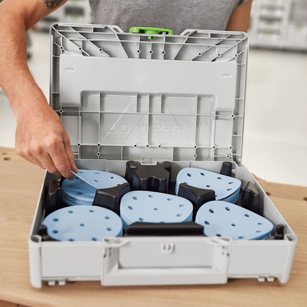 Festool Absaugmobil Cleantec mit aufgesetztem Systainer, in dem Schleifscheiben sortiert sind, bedient von einer knienden Person.