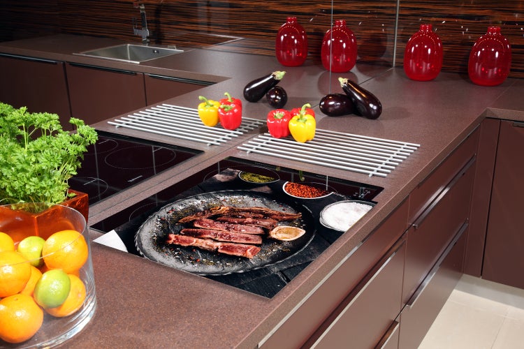 Küchenszene mit Lebensmitteln, Kochfeld und Küchenutensilien auf einer Arbeitsplatte.