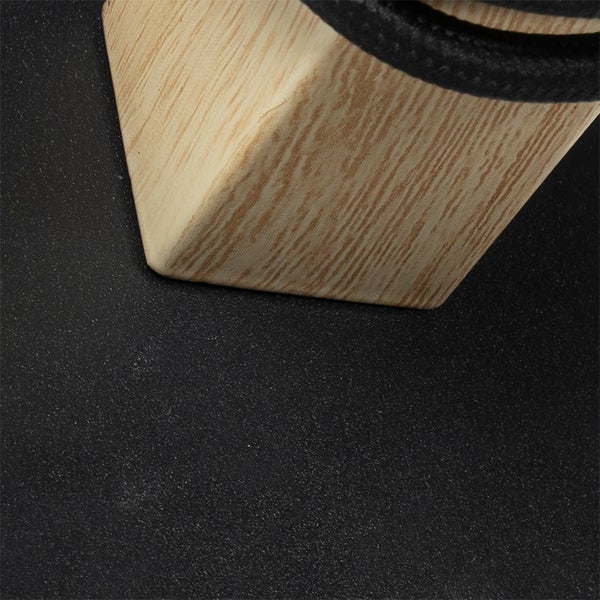 Detailansicht eines Tischbeins aus hellem Holz auf einer strukturierten dunklen Oberfläche.