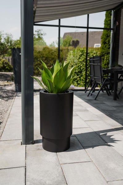 Moderner schwarzer zylindrischer Pflanzkübel mit Agave auf einer hellen gepflasterten Terrasse unter einer Überdachung in organisierter Atmosphäre.