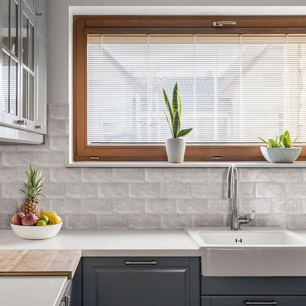 Moderne Küche mit Fliesenrückwand in Steinoptik, Holzfenster mit Jalousien, Keramikspüle und dunklen Küchenfronten in einer hellen Atmosphäre.