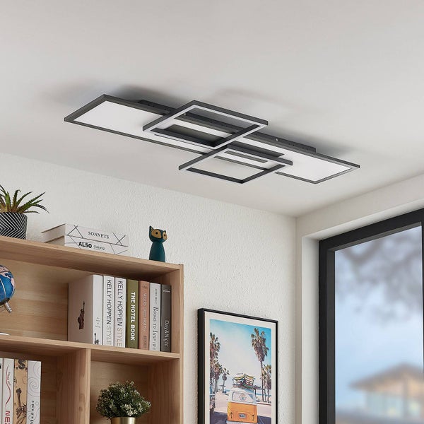 Moderne LED-Deckenleuchte mit geometrischen rechteckigen Rahmen über einem Bücherregal aus Holz in einem hellen Raum.