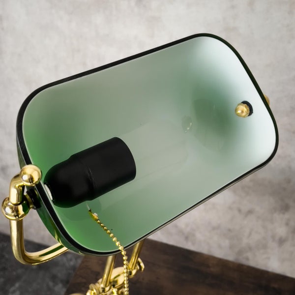 Detailansicht einer Schreibtischlampe mit grüner Glasabdeckung und Messingdetails.