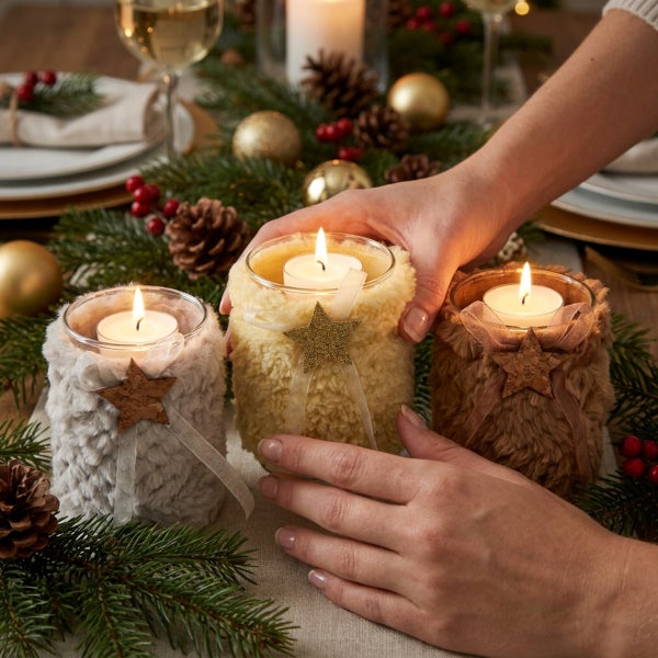 Drei Teelichthalter aus Glas mit flauschigem Überzug und Sternanhänger auf einem weihnachtlich dekorierten Tisch.