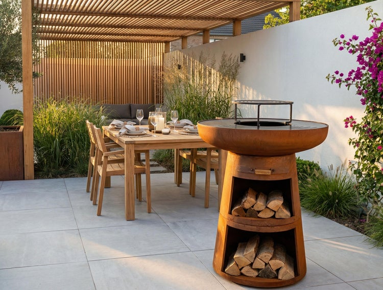 Moderner Terrassenbereich mit rundem Grill aus Cortenstahl inklusive Holzaufbewahrung, Holztisch mit Stühlen und einer Pergola.