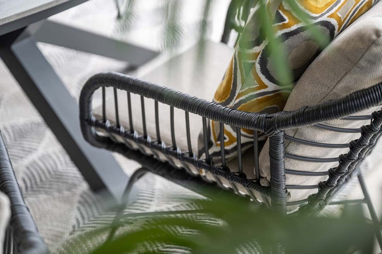 Detailansicht eines modernen Gartenstuhls mit Seilgeflecht an der Armlehne und einem Dekokissen.