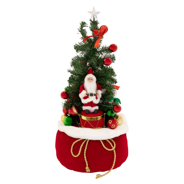 Geschmückter künstlicher Weihnachtsbaum mit Weihnachtsmannfigur auf einem Trommelsockel und einem großen Geschenkbeutel als Basis.