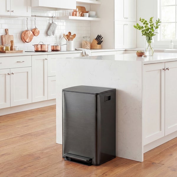 Schwarzer Tretmülleimer aus Metall in einer hellen, modernen Küche mit weißer Kücheninsel und Holzboden.