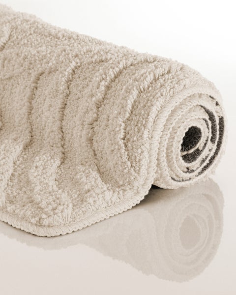 Beige aufgerollte Badematte mit weicher Hochflor-Oberfläche und Rippenstruktur.