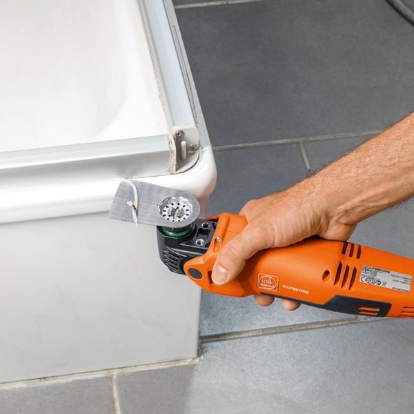Handwerker mit einem oszillierenden Multifunktionswerkzeug zum Schneiden von Silikonfugen an einer Badewanne
