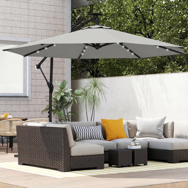 Großer rechteckiger Sonnenschirm über einem Lounge-Set aus Korbgeflecht auf einer hellen Terrasse mit Holzzaun und Bäumen im Hintergrund.