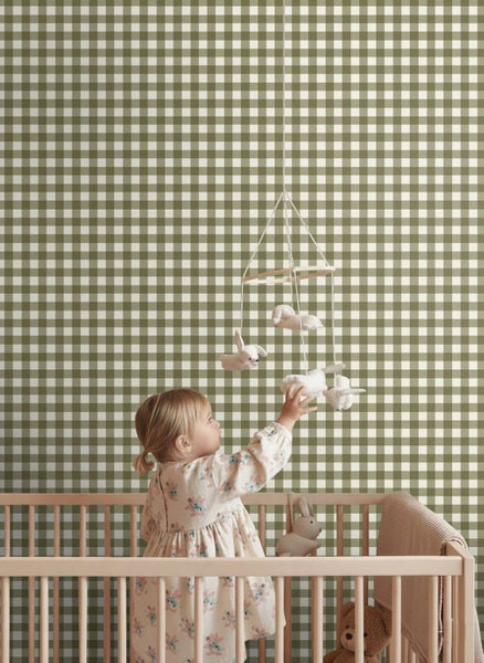 Vliestapete mit Gingham-Karomuster im Kinderzimmer hinter einem Holz-Gitterbett mit Baby und Mobile.