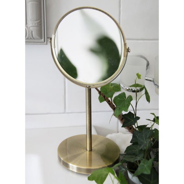 Runder Kosmetikspiegel in Goldoptik auf einem Waschtisch mit Pflanze