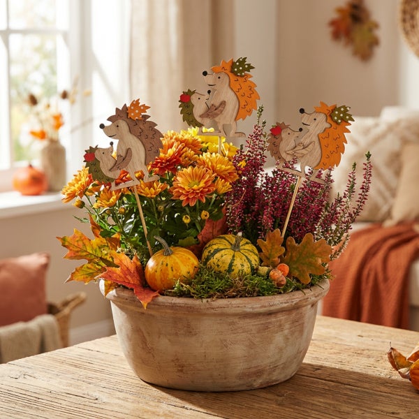 Herbstliche Blumenschale mit Chrysanthemen, Heidekraut, kleinen Kürbissen und dekorativen Holzsteckern in Igelform als herbstliche Tischdekoration.
