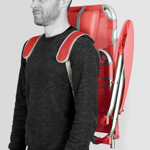 Zusammengeklappter roter Strandstuhl mit gepolsterten Rucksackgurten auf dem Rücken einer Person getragen.