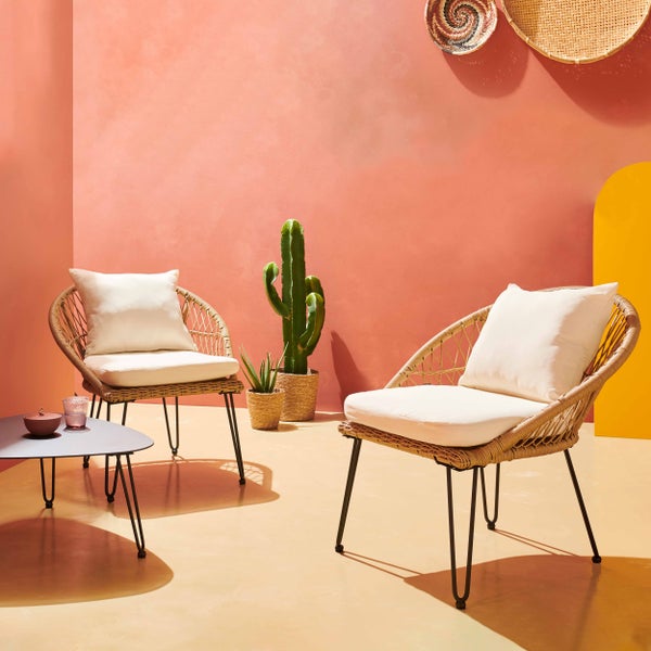 Helles Garten-Lounge-Set mit zwei Korbstühlen, weißen Sitzkissen, einem Beistelltisch, Kakteen und dekorativen Wandelementen aus Geflecht.