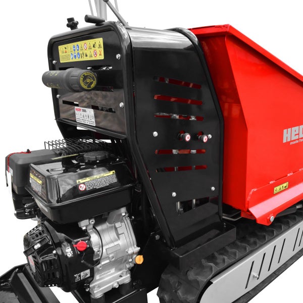 Detailansicht eines Raupendumpers mit Motor, Sicherheitssymbolen, einer roten Transportmulde und schwarzen Schutzblechen.