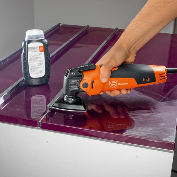 Eine Hand bedient einen Fein Multimaster auf einer Oberfläche, zusammen mit einer Flasche Politur.