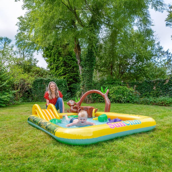Kind spielt im aufblasbaren SunClub Spielcenter im Garten, während eine Frau zuschaut.