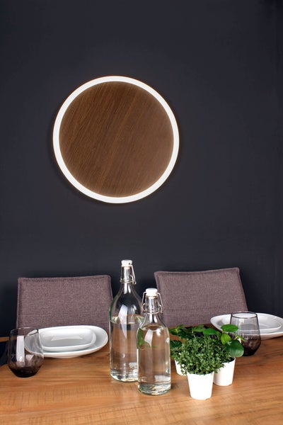 Runde LED Wandleuchte in Holzoptik mit leuchtendem Außenring in einem modern eingerichteten Esszimmer über einem gedeckten Holztisch.