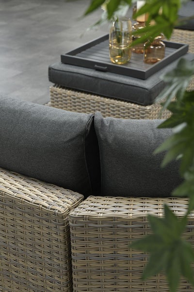 Nahaufnahme eines Garten-Loungemöbels aus hellem Polyrattan mit dicken anthrazitfarbenen Kissen.