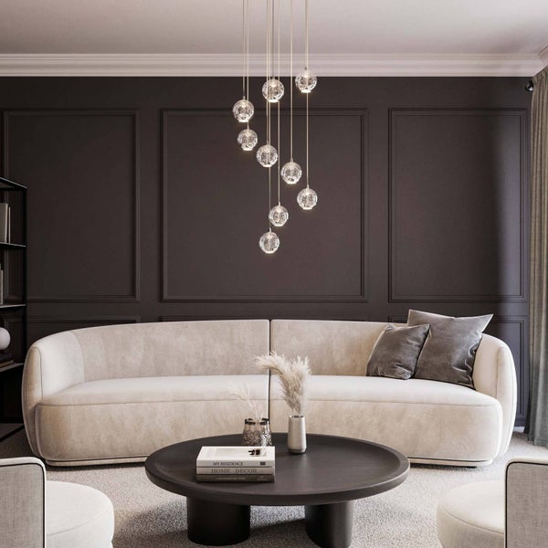 Moderne Pendelleuchte mit mehreren gläsernen Kugelschirmen in unterschiedlichen Höhen über einem Sofa in einem eleganten Wohnzimmer.