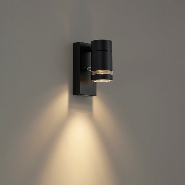 Schwarze Außenwandleuchte mit Bewegungsmelder, zylindrischer Kopf mit warmweißem Lichtstrahl nach unten.