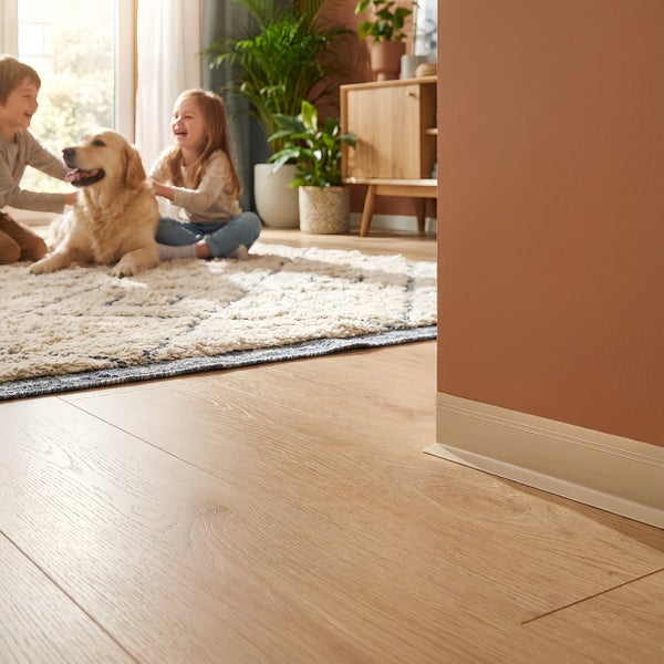 Heller Holzoptik Laminatboden mit Sockelleiste in einem wohnlichen Raum mit spielenden Kindern und einem Hund auf einem Teppich.