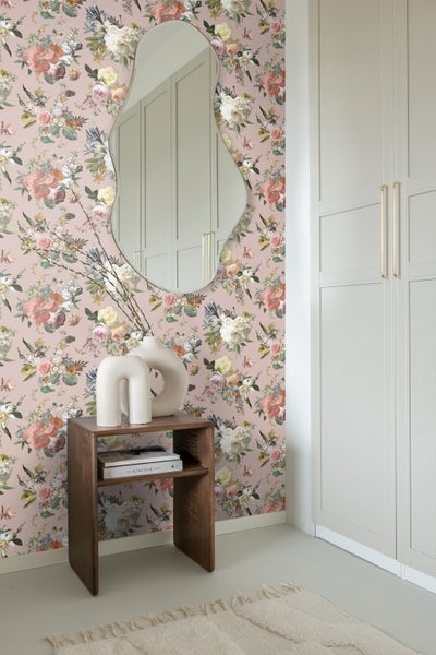 Helle Räumlichkeit mit Blumendekor-Tapete, Holzbeistelltisch, Spiegel und Garderobenschrank.