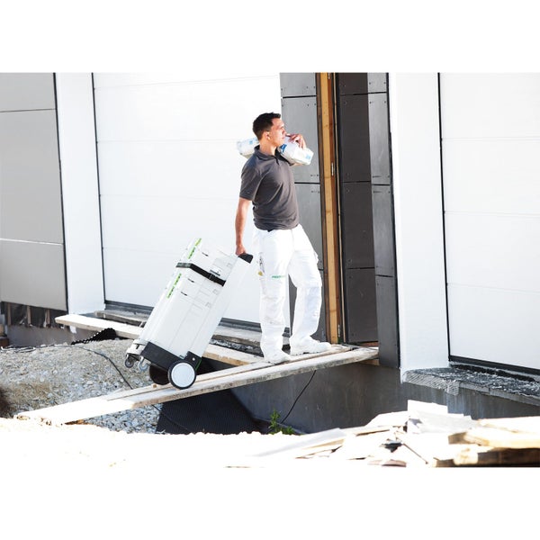 Mann transportiert Werkzeugkoffer und Sack Baumaterial zu einem Gebäude.