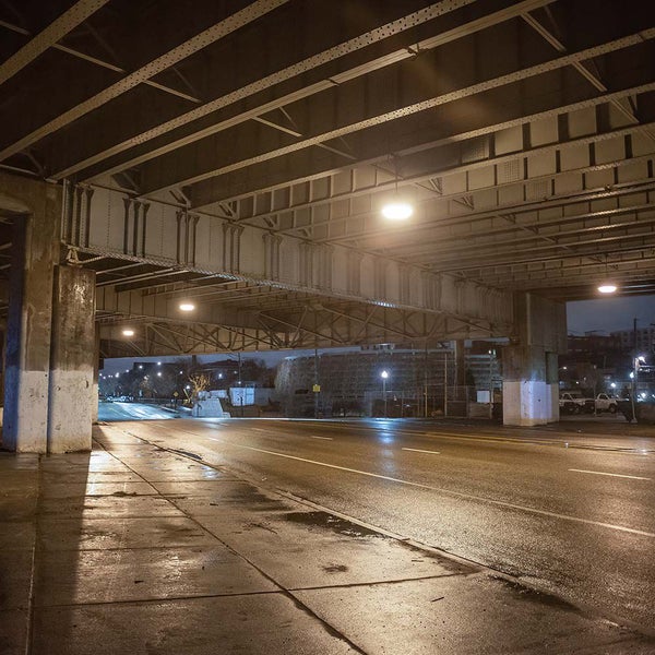 Beleuchtete Unterführung bei Nacht mit massiver Stahlträgerkonstruktion, Betonpfeilern und einer asphaltierten Straße.