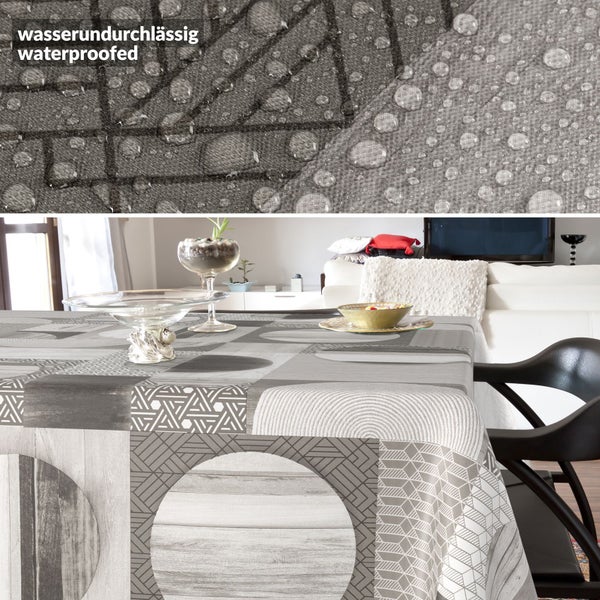 Wasserundurchlässige Tischdecke mit geometrischem Muster und Holzoptik in einem Wohnzimmer, Detailaufnahme zeigt Wassertropfen auf der Oberfläche.