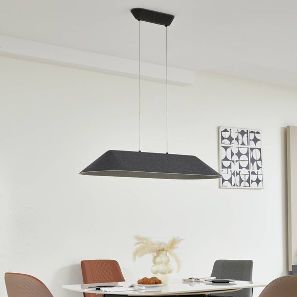 Moderne, längliche Pendelleuchte aus grauem Filz in einem hellen, minimalistischen Esszimmer über einem Esstisch.