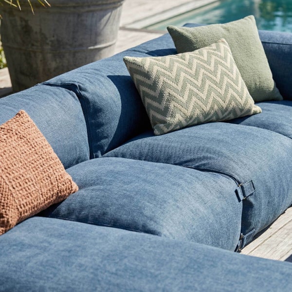 Modernes Outdoor-Lounge-Sofa aus blauem Stoff mit verschiedenen Zierkissen auf einer Holzterrasse am Pool.