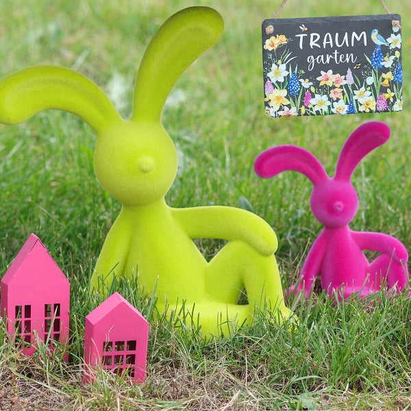Osterdekoration im Garten mit zwei beflockten Hasenfiguren zwei kleinen Häusern und einem Schild mit der Aufschrift Traumgarten.