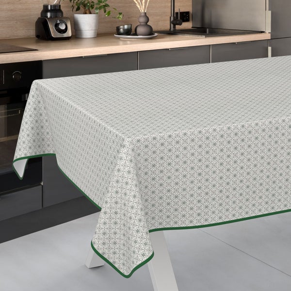 Tisch mit hell gemusterter Tischdecke und grüner Bordüre vor einer modernen Küchenzeile