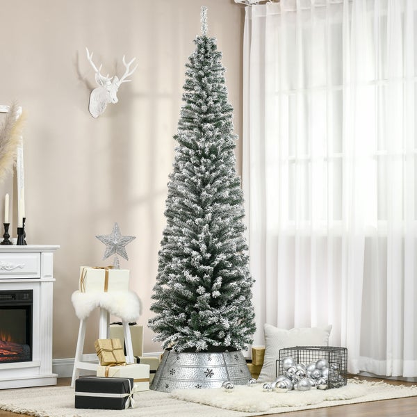 Schmaler künstlicher Weihnachtsbaum mit Schneeeffekt in einem hellen Wohnzimmer neben einem Kamin und Geschenken.