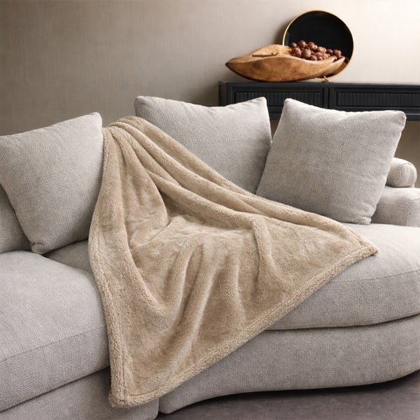 Eine weiche, flauschige Wohndecke auf einem modernen Sofa mit passenden Dekokissen in einem stilvoll eingerichteten Wohnbereich.