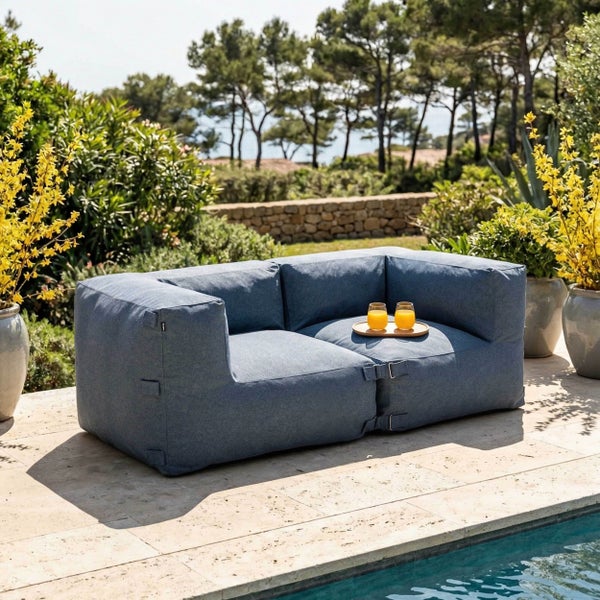 Modernes blaues Outdoor-Lounge-Sofa für zwei Personen auf einer Steinterrasse am Pool, umgeben von Pflanzen.