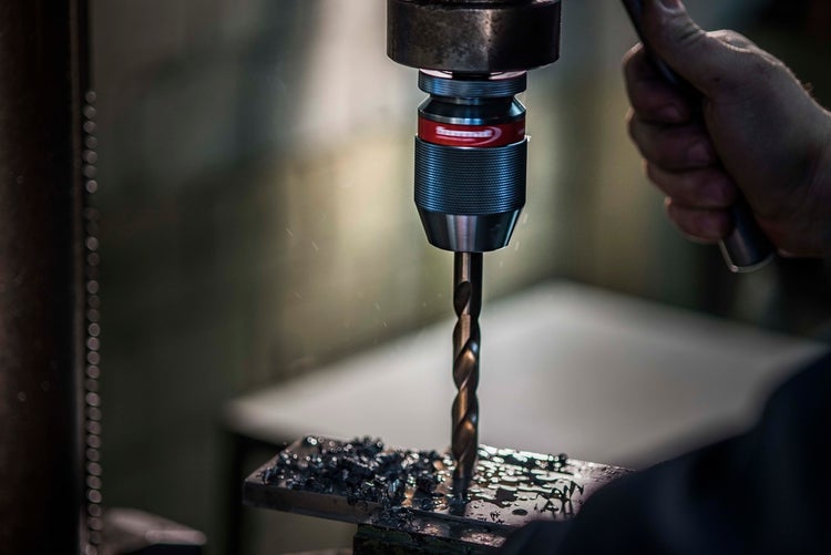 Tischbohrmaschine im Einsatz beim Bohren in ein Metallwerkstück mit sichtbaren Metallspänen.