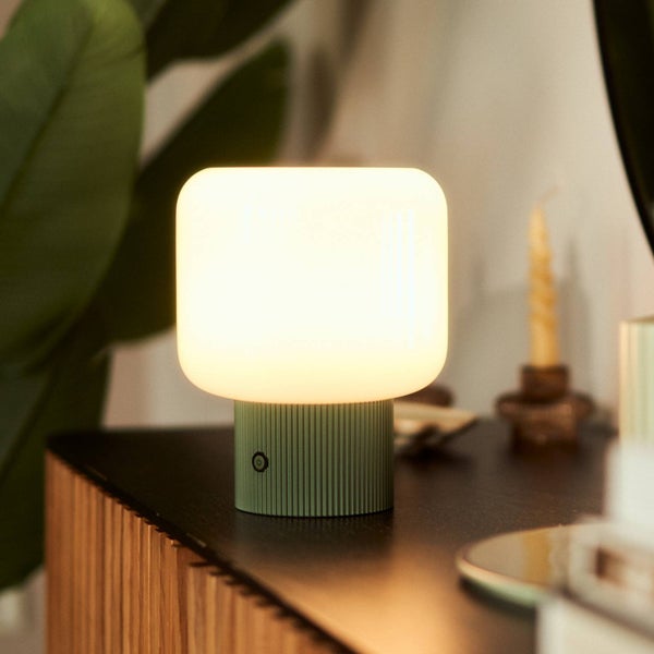 Moderne Tischleuchte mit grünem geriffeltem Sockel und weißem abgerundetem Lampenschirm, die warmes Licht auf einer dunklen Holzoberfläche verbreitet.