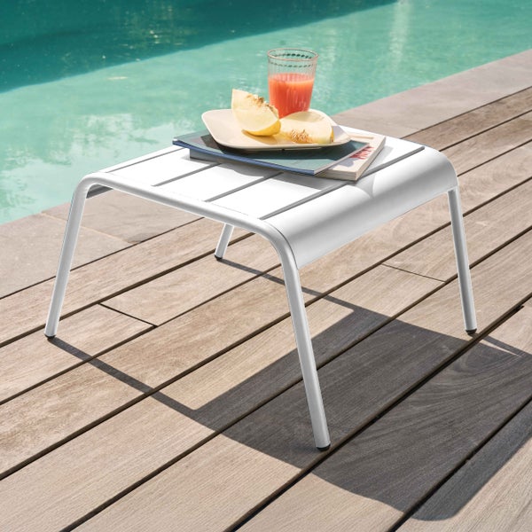 Weißer Garten-Beistelltisch aus Metall mit Lattenoberfläche auf einer Holzterrasse am Pool mit Getränk und Melone.