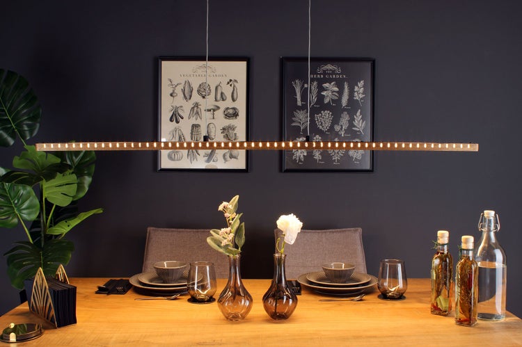 Moderne LED-Pendelleuchte aus Holz über einem gedeckten Esstisch in einem Esszimmer mit botanischen Wandbildern.